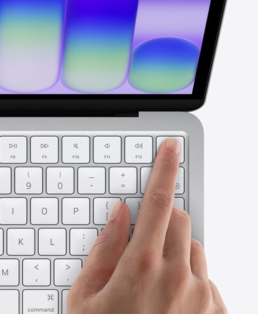 Hõbedane MacBook Neo, kellegi sõrm Touch ID anduril klaviatuuri ülemises paremas nurgas