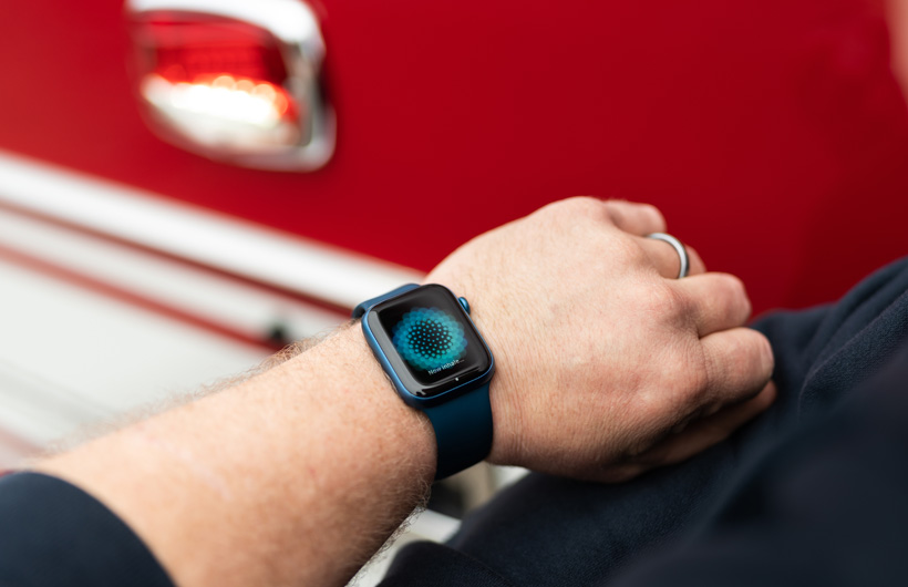 An arm wearing an Apple Watch displays the message: Now inhale, with a fire truck nearby