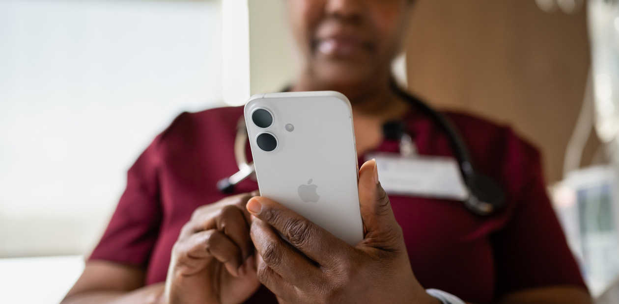 Une infirmière portant un uniforme rouge consulte son iPhone.