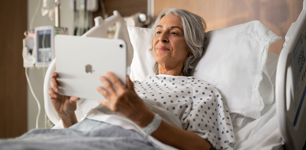 Une patiente couchée dans un lit d’hôpital consulte son iPad.