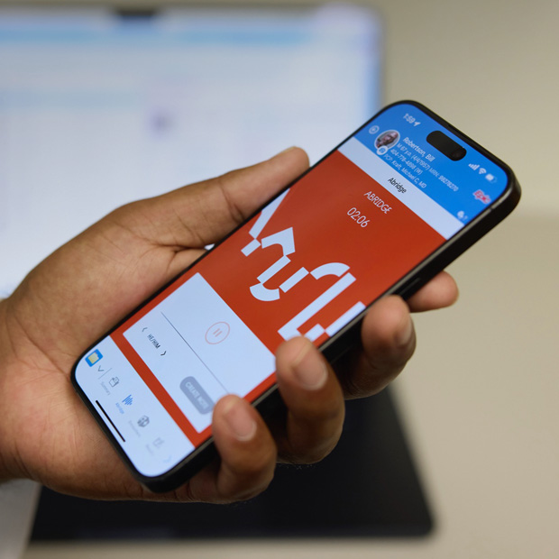 Une main tient un iPhone affichant l’app Abridge, qui transcrit les conversations entre les médecins et la patientèle en notes cliniques.