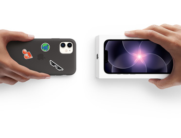 뒷면에 여러 스티커가 붙어 있는 실리콘 케이스 장착 iPhone 11을 들고 있는 손과 iPhone 17e용 새 iPhone 박스를 들고 있는 손이 서로 마주 보고 보상 판매를 하는 모습