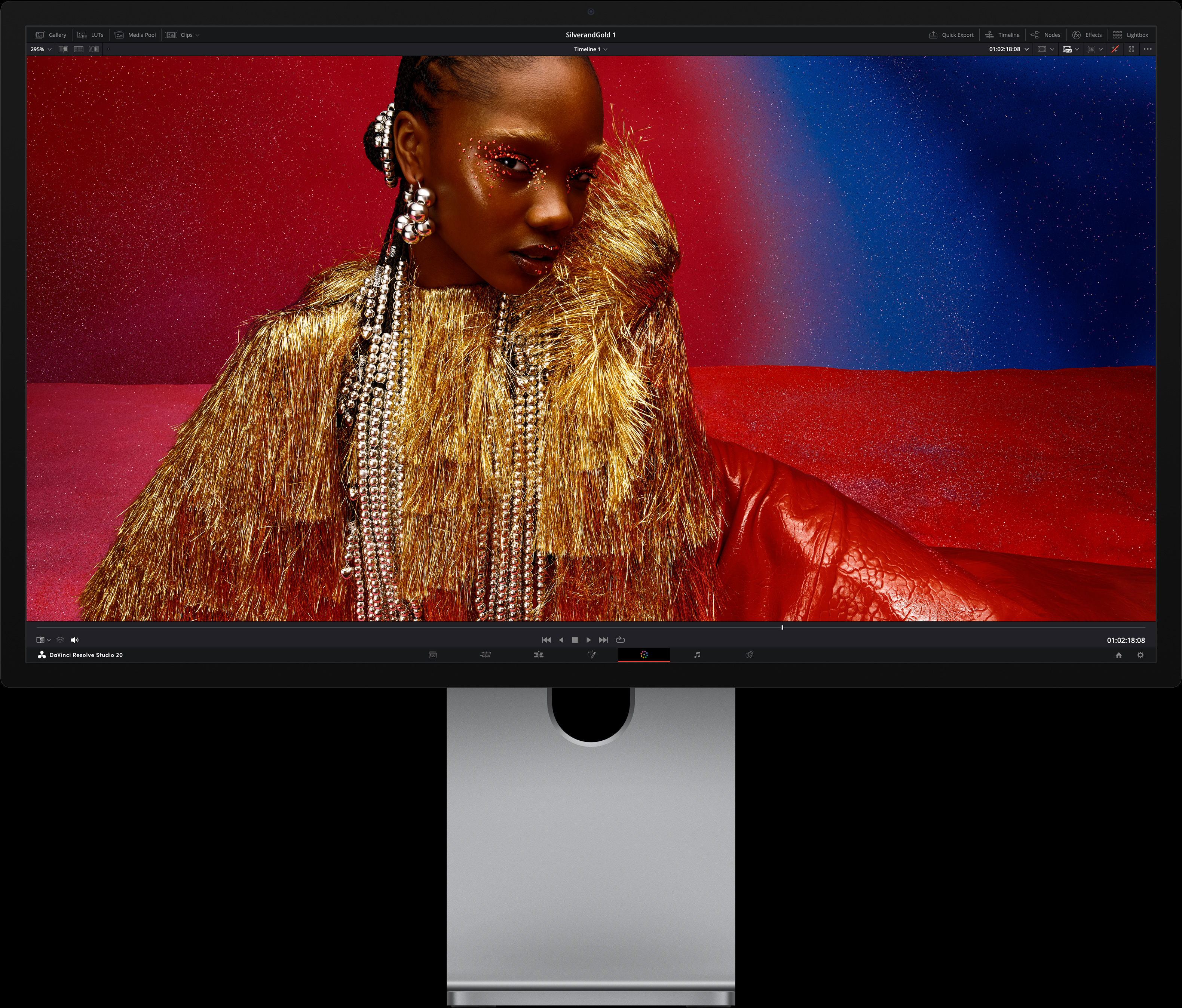 Ένα άτομο με φωτεινό κόκκινο φόρεμα και εντυπωσιακά μεταλλικά αξεσουάρ μπροστά σε μπλε και κόκκινο διαβαθμισμένο φόντο, αναδεικνύει την ποιότητα εικόνας του Studio Display XDR